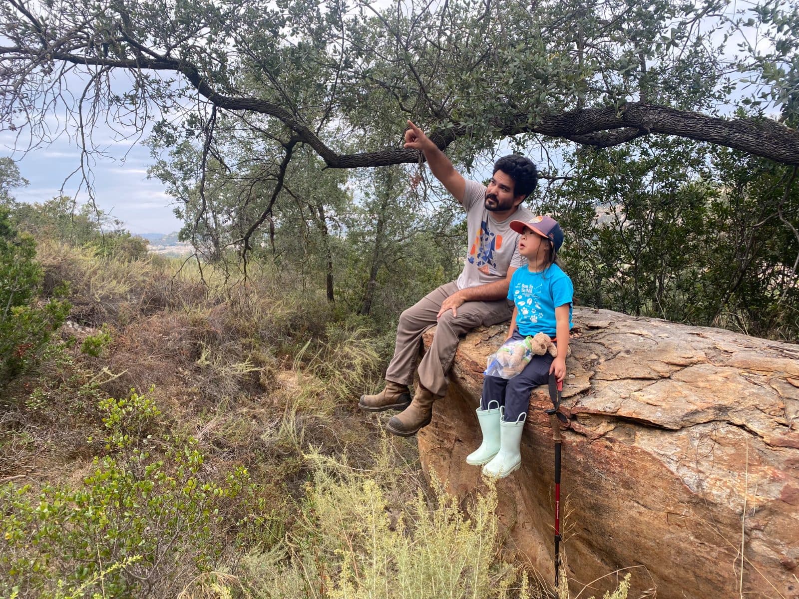 Jesse and our daughter sitting on a boulder under an oak tree