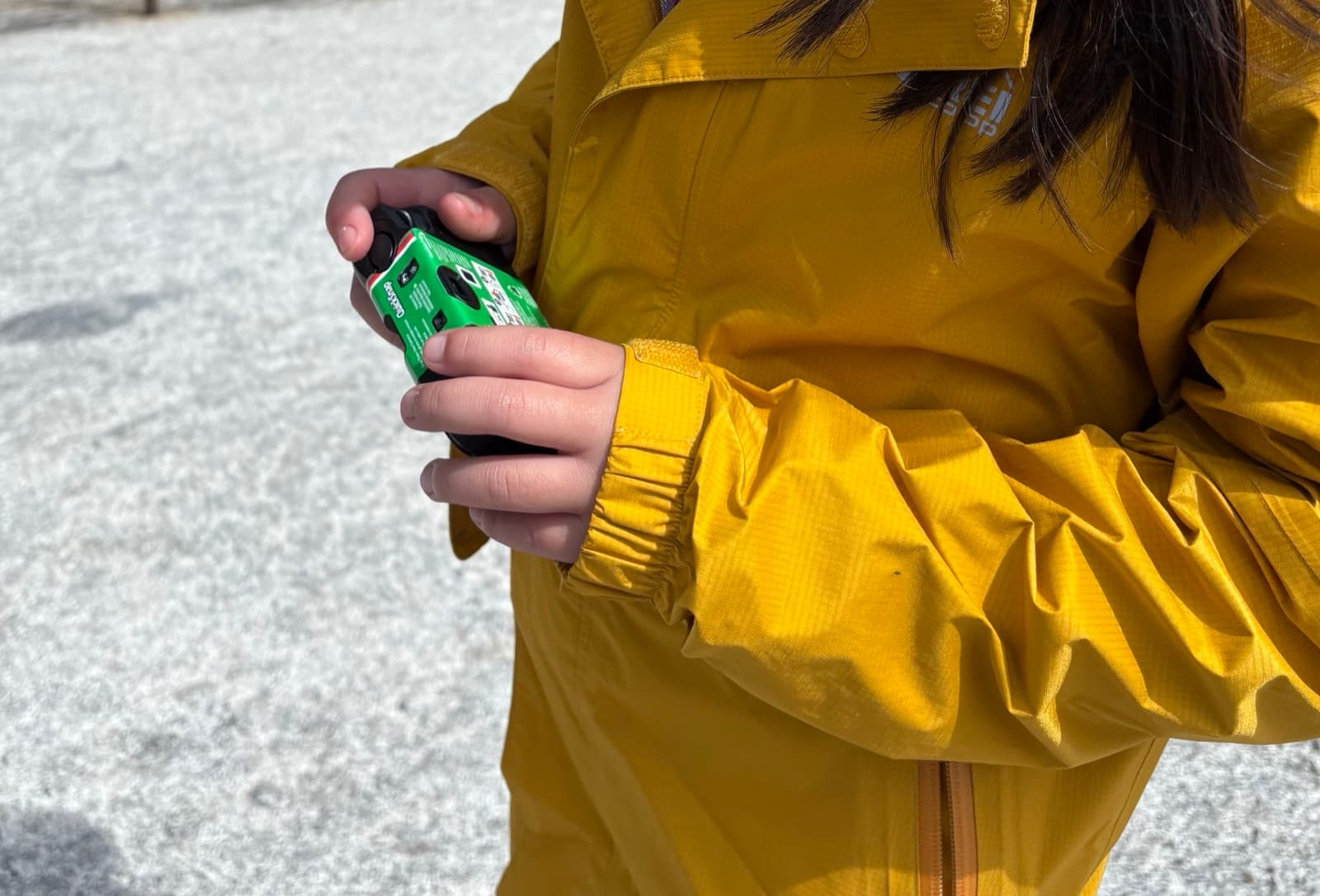 A student in a yellow rain jacket holding a disposable film camera